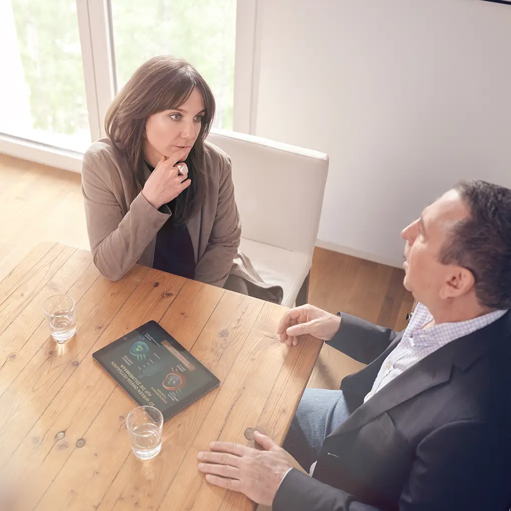 Janna Raphaela Odesser führt ein intensives Gespräch mit einem Patienten an einem Holztisch, auf dem ein Tablet mit grafischen Darstellungen liegt – fokussierte psychologische Arbeit in heller, ruhiger Umgebung