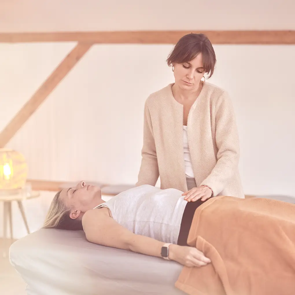 Janna Raphaela Odesser legt beruhigend die Hände auf den Bauch einer liegenden Person während einer Behandlung