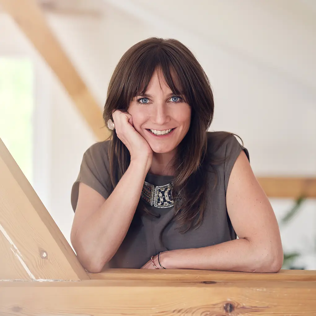 Janna Raphaela Odesser lehnt lächelnd an einer Holzbrüstung in einem hellen Raum